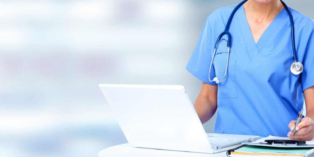 Nurse in scrubs standing in front of laptop.