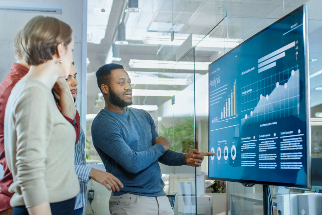 Group of colleagues looking at charts on large screen.